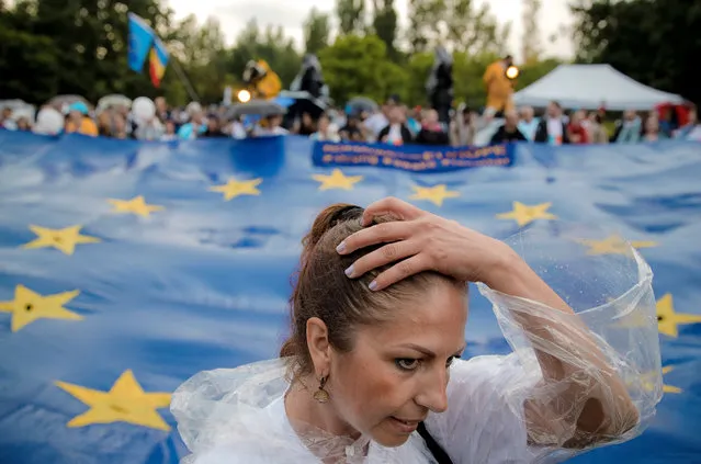 A woman runs her hand through her hair, backdropped by a European Union flag, during a 2020 USR PLUS alliance European Parliament elections rally, in Bucharest, Romania, Friday, May 24, 2019. Romanians will vote on Sunday, May 26, in the European Parliament elections. (Photo by Vadim Ghirda/AP Photo)