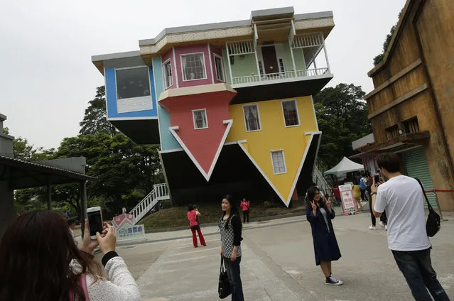 Visitors pose in front of a three story upside-down family sized house at the Huashan Creative Park in Taipei, Taiwan April 7, 2016. Over 300 square meters of floor space of the upside-down house, filled with home furnishings, was created by a group of Taiwanese architects at a total cost of around US$600,000 and took 2 months to complete, according to the organisers. (Photo by Tyrone Siu/Reuters)