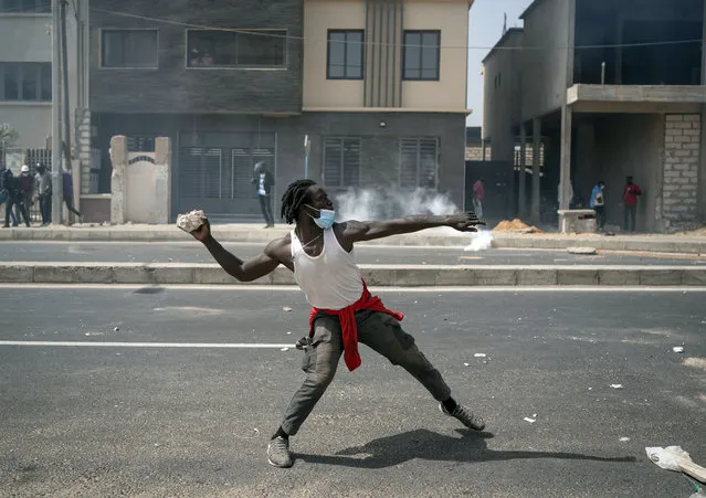 A demonstrator throws a rock at riot police during protests in support of main opposition leader and former presidential candidate Ousmane Sonko in Dakar, Senegal, Wednesday, March 3, 2021. Sonko was arrested Wednesday on charges of disturbing the public order after hundreds of his supporters clashed with police while he was heading to the court to face rape charges. (Photo by Leo Correa/AP Photo)