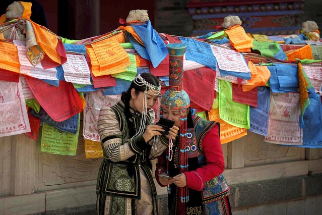 Tourists wearing Mongolian traditional costumes check on their souvenir photo taken at Dazhao Temple, a Tibetan Buddhist monastery during a five-day holiday for international labor day in Hohhot, north China's Inner Mongolia Autonomous Region, Thursday, May 2, 2024. (Photo by Andy Wong/AP Photo)
