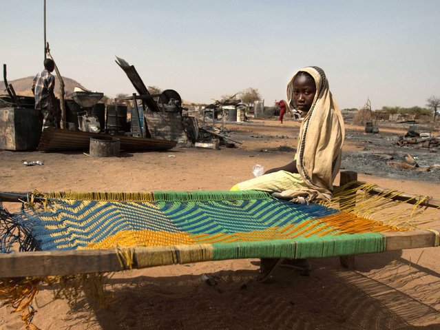 A displaced young girl sits on a makeshift bed in front of burnt houses in Khor Abeche, 83 km northeast on Nyala (South Darfur),  on April 6, 2014. Nearly 3000 people from Khor Abeche region in South Darfur leave their home and struggle to survive near the camp of United Nations Mission in Darfur (UNAMID) in Sudan. They are attacked by armed group on March 22 and they wait to be transfered to more safer region, Buzzer. (Photo by Albert Gonzalez Farran/AFP Photo)