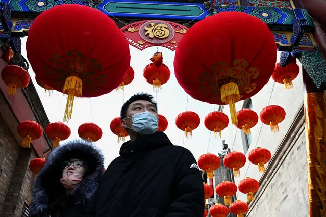 People walk under traditional lanterns a day before the start of the Lunar New Year, which ushers in the Year of the Tiger, along an alley in Beijing on January 31, 2022. (Photo by Noel Celis/AFP Photo)