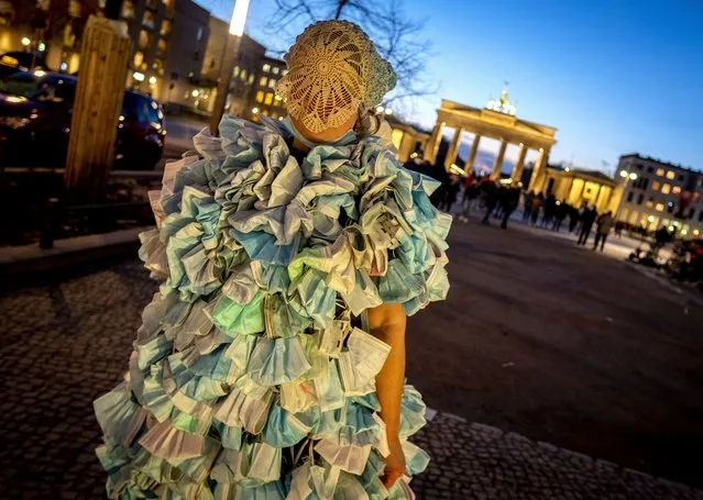 A woman wears a dress made of hundreds of face masks as she comes back from an anti corona demonstration in Berlin, Germany, Saturday, February 12, 2022. In background is the Brandenburg Gate. (Photo by Michael Probst/AP Photo)