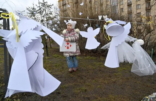 A girl looks at symbolic paper angels to pay tribute at the Maidan activists memorial also called the “Heroes of the Heavenly Hundred”, referring to the people killed during the anti-government demonstration of 2014, during a memorial event near the Independence Square, in Kyiv on February 18, 2022. Ukraine marksthe eighth anniversary of the bloody end to the revolution that ousted Russian-backed president Viktor Yanukovych and in which nearly 100 people were killed, most of them between February 18 and February 20, 2014. (Photo by Sergei Supinsky/AFP Photo)