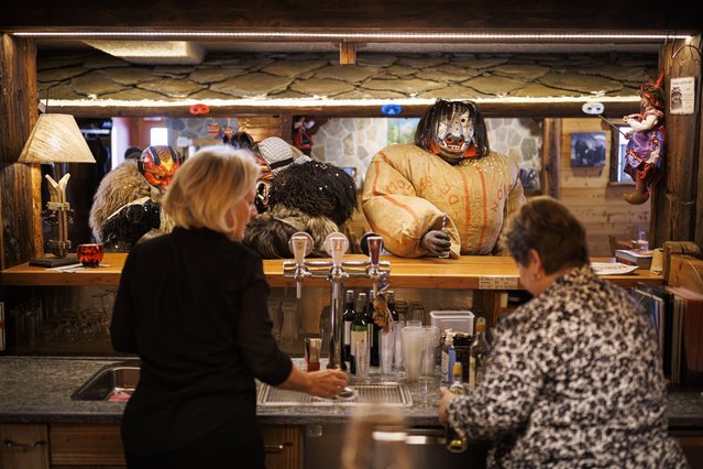 A man wearing a traditional straw stuffed costume enters a restaurant to ask for wine during the carnival through the alpine village of Evolene, Switzerland, 19 February 2023. The straw men, so-called “empailles” in French, stuffed with up to 30kg of straw, represent the spirit of the ancestors and deceased believed to haunt the region. (Photo by Valentin Flauraud/EPA)