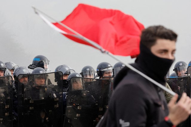 Police officers in riot gear stand guard as French workers on strike gather and block the entry of a fuel depot as they protest against the French government's pension reform plan, in Haulchin, near Valenciennes, France on March 13, 2023. (Photo by Pascal Rossignol/Reuters)