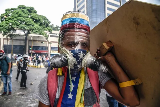 A Venezuelan opposition activist wearing a homemade gas mask takes cover behind a makeshift shield as clashes erupt with riot police during a protest against President Nicolas Maduro, in Caracas on May 8, 2017. Venezuela's opposition mobilized Monday in fresh street protests against President Nicolas Maduro's efforts to reform the constitution in a deadly political crisis. Supporters of the opposition Democratic Unity Roundtable (MUD) gathered in eastern Caracas to march to the education ministry under the slogan “No to the dictatorship”. (Photo by Juan Barreto/AFP Photo)