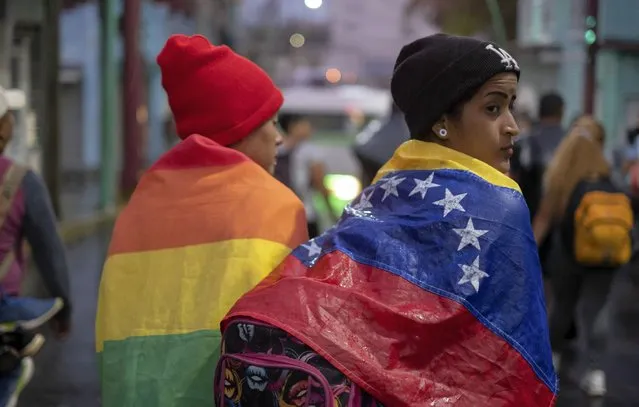 A person draped in a Venezuelan flag walks with a group of migrants walking out of the city of Tapachula in Chiapas state, Mexico, early Monday, June 6, 2022. Several thousand migrants set out walking in the rain early Monday in southern Mexico, tired of waiting to normalize their status in a region with little work still far from their ultimate goal of reaching the United States. (Photo by Isabel Mateos/AP Photo)