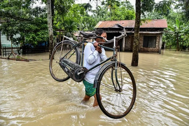 A man carries his bicycle as he wades through flood waters in Solmara of Nalbari district, in India's Assam state on June 19, 2022. (Photo by Biju Boro/AFP Photo)