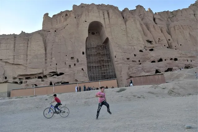 In this picture taken on July 13, 2022, children play at the site where the Shahmama Buddha statue once stood before being destroyed by the Taliban in March 2001, in Bamiyan province. (Photo by Ahmad Sahel Arman/AFP Photo)