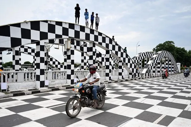 Boys stand on an arch of Napier bridge painted as chessboard on the occasion of Chess Olympiad 2022, which will be held from 28 July to 10 August, in Chennai on July 26, 2022. (Photo by Arun Sankar/AFP Photo)