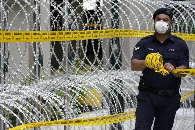 A police officer sets up perimeter at a building under lockdown in Kuala Lumpur, Malaysia, Wednesday, April 15, 2020. The Malaysian government issued a restricted movement order to the public till April 28, to help curb the spread of the new coronavirus. (Photo by Vincent Thian/AP Photo)
