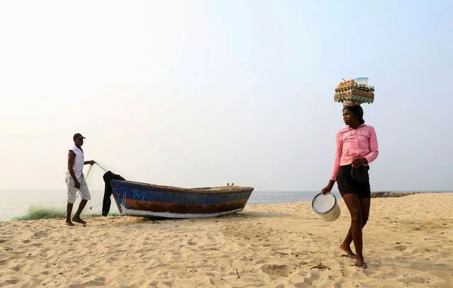 A woman selling eggs walks past a man preparing his boat, in Luanda, Angola on  August 25, 2022. (Photo by Siphiwe Sibeko/Reuters)