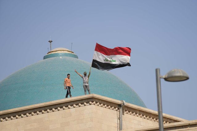 Supporters of Shiite cleric Muqtada al-Sadr wave a national flag from the roof of the Government Palace during a demonstration in Baghdad, Iraq, Monday, August 29, 2022. Al-Sadr, a hugely influential Shiite cleric announced he will resign from Iraqi politics and his angry followers stormed the government palace in response. The chaos Monday sparked fears that violence could erupt in a country already beset by its worst political crisis in years. (Photo by Hadi Mizban/AP Photo)