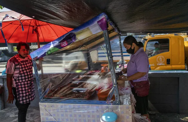 A street food vender standing behind plastic sheets to help curb the spread of the new coronavirus prepares a meal in Bangkok, Thailand, Tuesday, April 28, 2020. (Photo by Gemunu Amarasinghe/AP Photo)