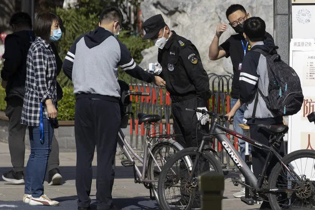 A security guard takes the temperature of a student arriving for the reopening of school at a middle school in Beijing on Monday, May 11, 2020. The Chinese capital partially reopen schools for some students on Monday as authorities push to restore normalcy after the lockdown to fight the coronavirus. (Photo by Ng Han Guan/AP Photo)
