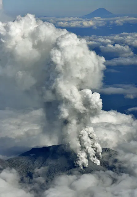 Dense fumes are spewed out from Mt. Ontake as the volcano erupts in central Japan Saturday, September 27, 2014. Mt. Ontake erupted Saturday, sending a large plume of ash high into the sky and prompting a warning to climbers and others to avoid the area. Japanese broadcaster NHK, citing local authorities, said there were reports of injuries, but no word on their severity. It also reported that people had been evacuated from a mountain lodge. Mount Fuji, Japan's tallest mountain, is seen at top right. (Photo by AP Photo/Kyodo News)