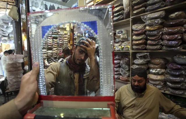 A customer tries a traditional cap for the upcoming Eid al-Fitr holiday that marks the end of the Muslim holy fasting month of Ramadan after the government relaxed a weeks-long lockdown that was enforced to help curb the spread of the coronavirus, in Peshawar, Pakistan, Friday May 22, 2020. (Photo by Muhammad Sajjad/AP Photo)