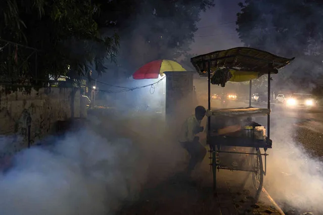 A street vendor tries to avoid fumes as a municipal worker fumigates a residential area to prevent mosquitoes from breeding in Prayagraj, in the northern state of Uttar Pradesh, India, Wednesday, October 12, 2022. Officials say infections following monsoon rains have led to a fever outbreak in this northern state. (Photo by Rajesh Kumar Singh/AP Photo)