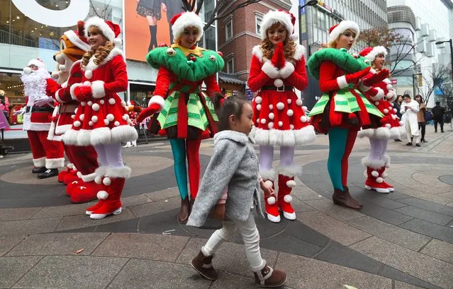A girl walks in front of performers clad in Santa Claus outfits during a street event to promote Christmas season at a shopping district in Seoul on November 13, 2017. South Korean young people enjoy celebrating the Christmas season though the majority of residents are Buddhists. (Photo by Jung Yeon-Je/AFP Photo)