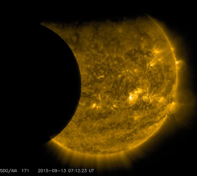 This September 13, 2015 image provided by NASA shows the moon, left, and the Earth, top, transiting the sun together, seen from the Solar Dynamics Observatory. The edge of Earth appears fuzzy because the atmosphere blocks different amounts of light at different altitudes. This image was taken in extreme ultraviolet wavelengths, invisible to human eyes, but here colorized in gold. (Photo by NASA/SDO via AP Photo)
