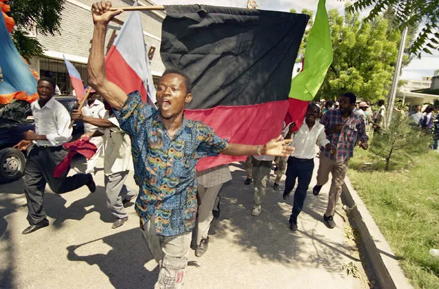 Haitian armed civilians, called attaches, run through a Port-au-Prince street carrying the black and red flag of former dictator Francois Papa Doc Duvalier as they demonstrate against the return of ousted Haitian President Jean-Bertrand Aristide and against the U.N. mission in downtown Port-au-Prince, Haiti on Friday, October 8, 1993. Aristide is scheduled to be returned to power by the end of October. (Photo by Michael Stravato/AP Photo)
