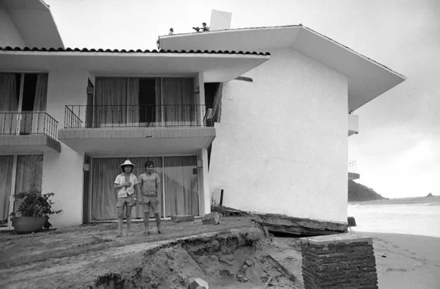 Hotel El Presidente, located in the beach resort town of Ixtapa, tilts precariously toward the Pacific Ocean after a tidal wave brought on by hurricane Madeline ate away the foundations. Two men in foreground survey the damage. Madeline came ashore near Ixtapa, Mexico on Friday, October 9, 1976, killing at least two persons and injuring nine others. (Photo by AP Photo/HEM)