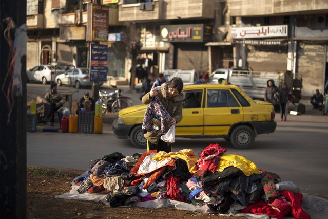 A women looks at second hand clothes displayed on a street for sale near an Alawite neighbourhood, in Homs, Syria, Thursday, December 26, 2024. (Photo by Leo Correa/AP Photo)