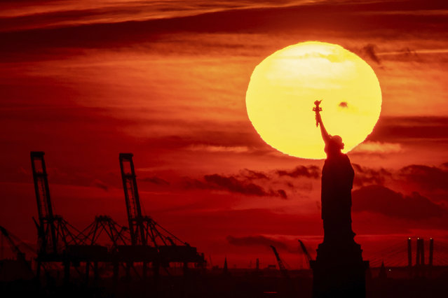The sun sets behind the Statue of Liberty, Thursday, November 17, 2022, in New York. (Photo by Julia Nikhinson/AP Photo)