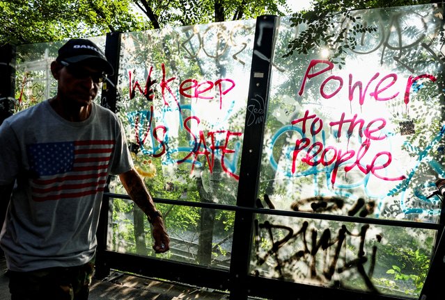 A man walks by graffiti on a pedestrian bridge reading “We keep us safe” and “Power to the people” after President Trump announced a federal takeover of the Metropolitan Police Department, in Washington, on August 12, 2025. (Photo by Jonathan Ernst/Reuters)