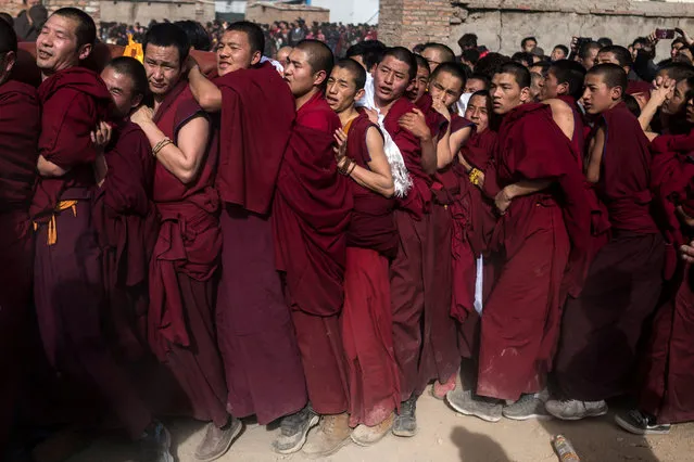 This picture taken on March 1, 2018 shows Tibetan Buddhist monks carrying a giant thangka for the unveiling ceremony during Monlam, otherwise known as the Great Prayer Festival of Losar, the Tibetan New Year, at the Rongwo Monastery, in Tongren County, Huangnan Tibetan Autonomous Prefecture, on the Qinghai- Tibet plateau. Scores of monks and men heaved the enormous thangka – an image of Buddha painted on silk, rolled up in a tight cylinder while in transit – through the packed streets around Rongwo Monastery in China's northwestern province of Qinghai for a religious ritual wrapping up Losar, the Tibetan new year. (Photo by Johannes Eisele/AFP Photo)
