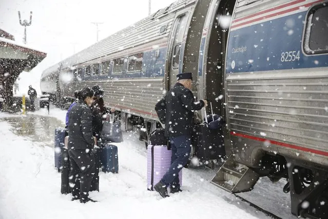 The conductor helps passengers board the southbound Amtrak Vermonter in Waterbury, Vt., during a snowstorm on Tuesday, March 14, 2023. The train was traveling during a winter storm that was dropping heavy, wet snow across the Northeast. The storm caused a plane to slide off a runway, led to hundreds of school closings, canceled flights and thousands of power outages in parts of the Northeast on Tuesday. (Photo by Wilson Ring/AP Photo)
