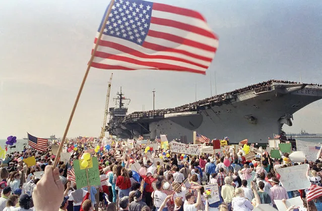 A crowd estimated at 35,000 friends, family and wellwishers wave flags and signs as they welcomed the aircraft carrier USS John F. Kennedy to the Norfolk Naval Base in Norfolk, Thursday, March 28, 1991. Ten thousand sailors in the eight ship Kennedy battle group returned to their homeport of Norfolk after a 7 month deployment on Operation Desert Storm. (Photo by Steve Helber/AP Photo)