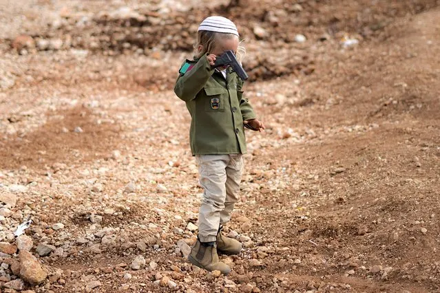Yossef, a Jewish settler boy, wears costumes as an Israeli soldier, as he plays with a toy gun during the Jewish festival of Purim, next to Tapuach junction checkpoint, not far from the Palestinians city of Nablus, Tuesday March 7, 2023. The Jewish holiday of Purim commemorates the Jews salvation from genocide in ancient Persia, as recounted in the Book of Esther. (Photo by Ariel Schalit/AP Photo)