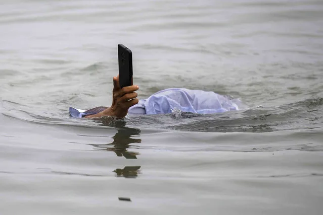 A Hindu devotee takes a dip while holding his mobile phone above water in the river Brahmaputra in Guwahati, India, Wednesday, March 22, 2023. From droughts stifling once-reliant sources to destructive downpours and floods, what the world does about its water woes is the central question at the U.N.'s three-day water conference that begins Wednesday which also marks the 30th anniversary of World Water Day. (Photo by Anupam Nath/AP Photo)