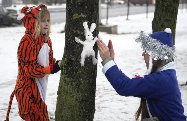 Girls dressed in Christmas costumes of a Snow Maiden and a tiger sculpt a snow hare on a tree in St. Petersburg, Russia, Saturday, December 19, 2020. (Photo by Dmitri Lovetsky/AP Photo)
