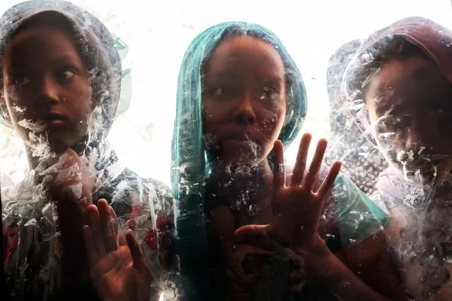 Girls are seen through a glass at the compound of the Agda Hotel, in the city of Semera, Afar region, Ethiopia, on February 14, 2022. Thousands of Eritrean refugees, shell-shocked and separated from loved ones, fled on foot through harsh terrain to escape artillery and gunfire. (Photo by Eduardo Soteras/AFP Photo)
