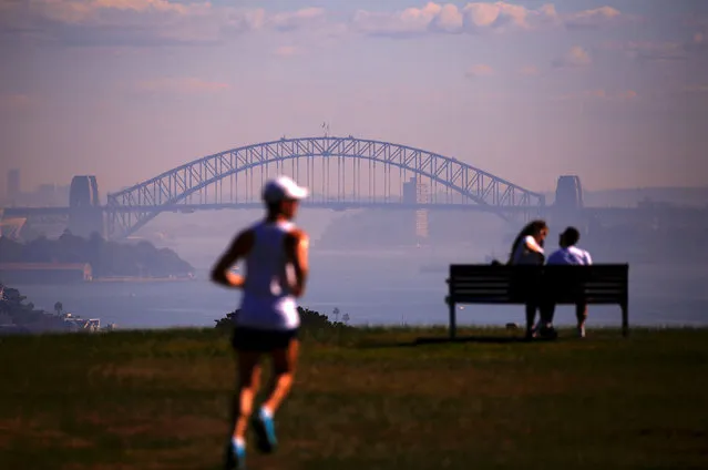 A man runs near a couple sitting on a seat overlooking Sydney Harbour, which was covered in smoke from hazard reduction burns of bushland around the city of Sydney, in Australia, May 29, 2018. (Photo by David Gray/Reuters)