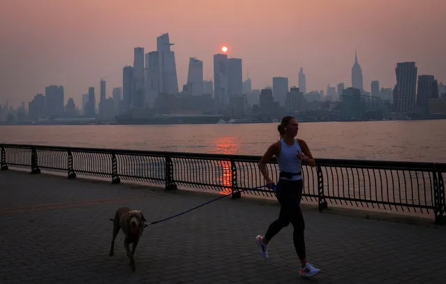 A woman jogs with a dog along the Hudson River shortly after sunrise, as haze and smoke caused by wildfires in Canada hang over the Manhattan skyline, in New York City, New York, U.S., June 7, 2023. (Photo by Mike Segar/Reuters)