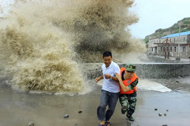 A frontier soldier helps a man move away from waves ahead of Typhoon Soulik in Wenzhou, Zhejiang province, China, on July 14, 2013. (Photo by Reuters/China Daily)