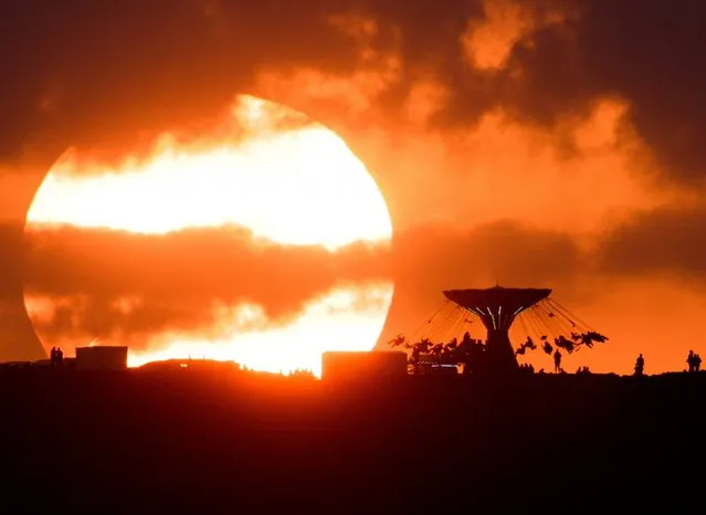 Revellers enjoy a ride while the sun sets behind a fair ground in Sehnde, near Hanover, Germany, August 20, 2016. This image was made using a super-telephoto lens. (Photo by Julian Stratenshulte/EPA)