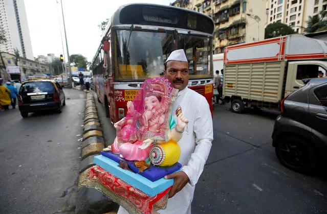 A man carries an idol of Hindu god Ganesh, the deity of prosperity, on the first day of the ten-day-long Ganesh Chaturthi festival, as he waits to cross a road in Mumbai, India, September 13, 2018. (Photo by Francis Mascarenhas/Reuters)