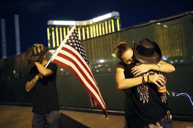 Megan Murphy, right in hat, embraces Cara Knoedler as Kenneth Wright wipes his eyes on the first anniversary of the mass shooting, Monday, October 1, 2018, in Las Vegas. Behind them is the site of the shooting. Hundreds of survivors of the Las Vegas mass shooting have formed a human chain around the shuttered site of a country music festival where a gunman opened fire Oct. 1, 2017. (Photo by John Locher/AP Photo)