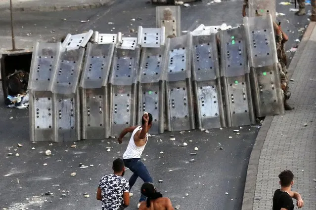 A supporter of Prime Minister-designate Saad Hariri who stepped down on Thursday, throws stones against Lebanese soldiers who hide behind their protective shield, in Beirut, Lebanon, Thursday, July 15, 2021. Hariri says he is stepping down, nine months after he was named to the post by the parliament. He is citing “key differences” with the country's president, Michel Aoun. (Photo by Hussein Malla/AP Photo)