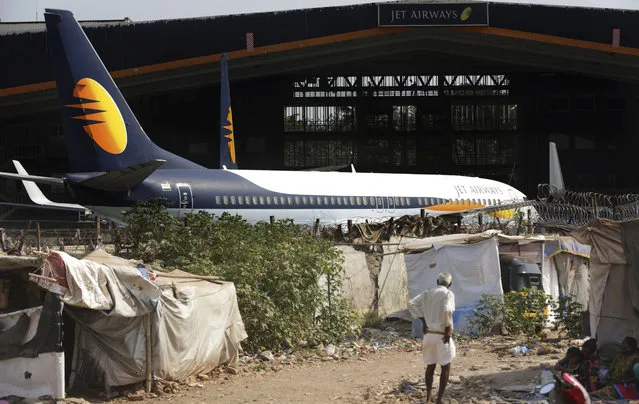 A man stands next to his shanty as Jet Airways aircraft is seen parked at a hanger at Chhatrapati Shivaji Maharaj International Airport in Mumbai, Monday, March 25, 2019. The chairman of India’s private Jet Airways has quit amid mounting financial woes forcing the airline to suspend operations on 14 international routes with more than 80 planes grounded. (Photo by Rafiq Maqbool/AP Photo)
