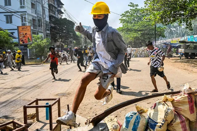 In this file photo taken on March 19, 2021, a protester jumps over a makeshift barricade during a crackdown by security forces on a demonstration against the military coup in Yangon's Thaketa township. Myanmar's military seized power on February 1, ousting the civilian government and arresting its leader Aung San Suu Kyi -- the 100 days that followed have seen mass street protests, bloody crackdowns by the junta, economic turmoil and growing international concern. (Photo by AFP Photo/Stringer)
