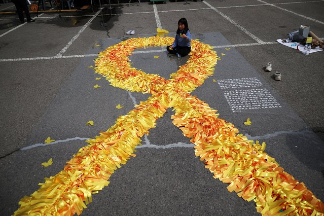 A girl sits inside a large yellow coloured ribbon dedicated to victims of the sunken Sewol ferry disaster that killed 304 people, mostly school students, during a ceremony to commemorate its tenth anniversary in Ansan, South Korea, on April 16, 2024. (Photo by Kim Hong-Ji/Reuters)