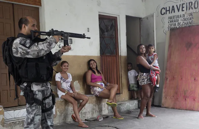 Residents observe a police officer take up position during an operation at the Mare slums complex in Rio de Janeiro March 25, 2014. (Photo by Ricardo Moraes/Reuters)