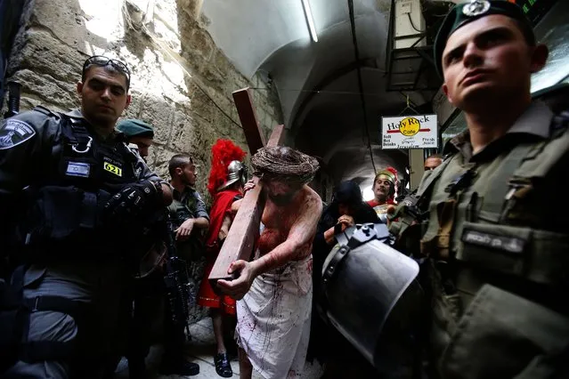 Israeli security force stand guard as Christian pilgrim reenacts the Passion of Christ along the Via Dolorosa (Way of Suffering) during a procession marking Good Friday on April 18, 2014 in Jerusalem's old city. Thousands of Christian pilgrims take part in processions along the route where, according to tradition, Jesus Christ carried the cross during his last days, as Christians around the world mark the Holy Week, commemorating the crucifixion of Jesus Christ, leading up to his resurrection on Easter. (Photo by Gali Tibbon/AFP Photo)