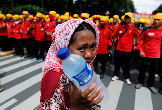 A street vendor holds drinking water as she walks near workers attending a May Day rally in front of presidential palace in Jakarta, Indonesia, May 1, 2016. (Photo by Reuters/Beawiharta)